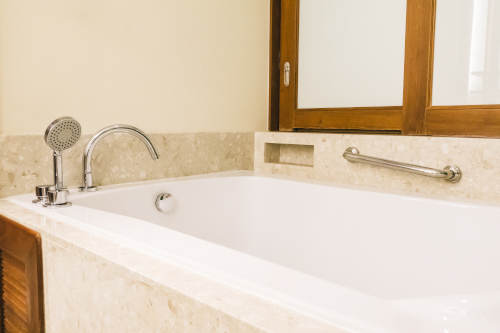 Bathtub decoration in bathroom interior Elegant built-in bathtub with beige marble surround and handheld faucet