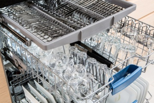 Open dishwasher with clean utensils in it. Interior of modern dishwasher loaded with glassware, dishes, and cutlery