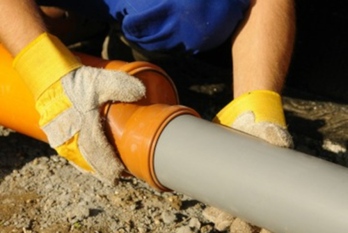 underground-plumbing-pipe-connection-by-worker Worker installing underground plumbing with orange and gray pipe joints