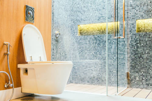 wall-mounted-toilet-and-walk-in-shower-with-tile-wall Wall-mounted toilet beside a walk-in shower with glass doors and mosaic tiles
