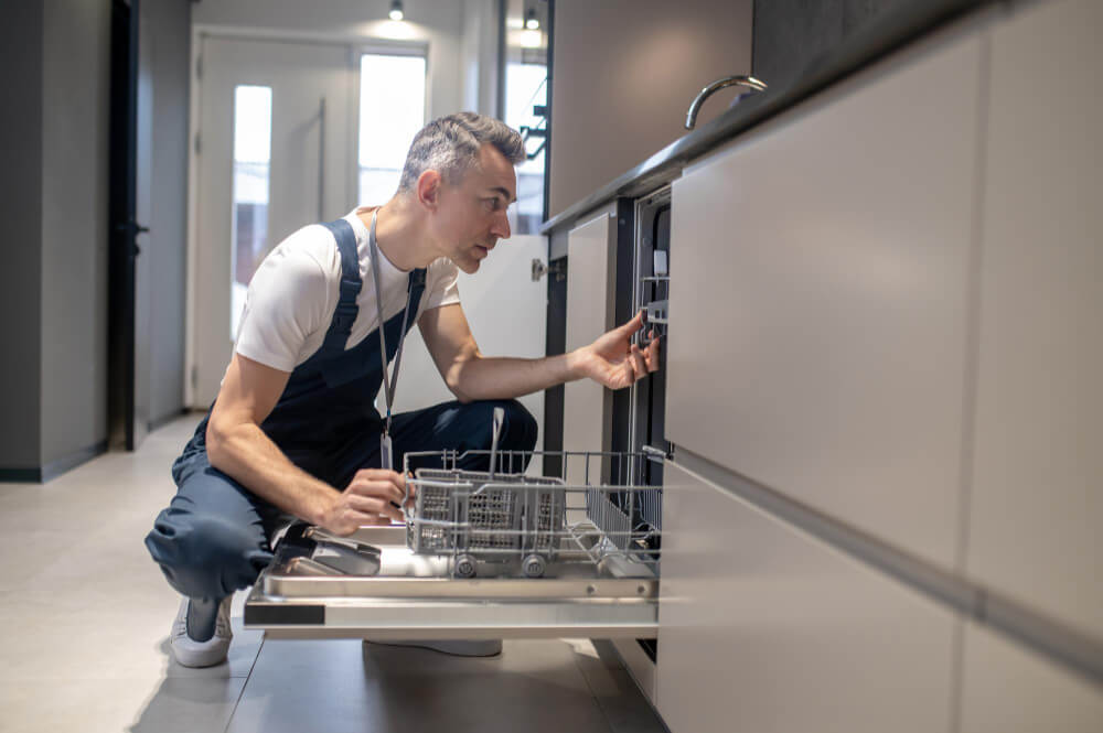 A man installing a dishwasher in a modern kitchen.